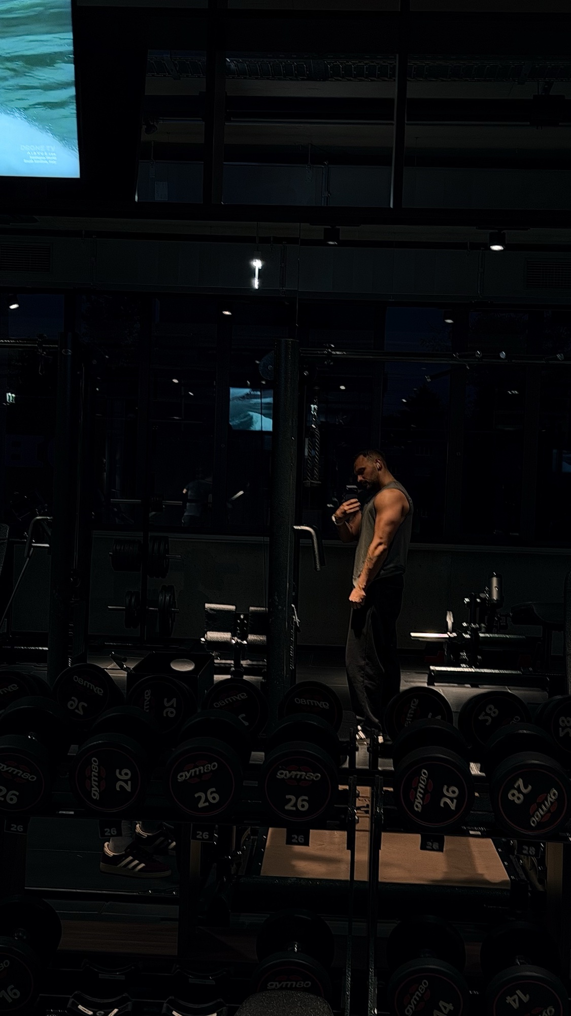 Neues Trainingsfoto im dunklen Studio zwischen Hantelreihen, mit kühlem Licht